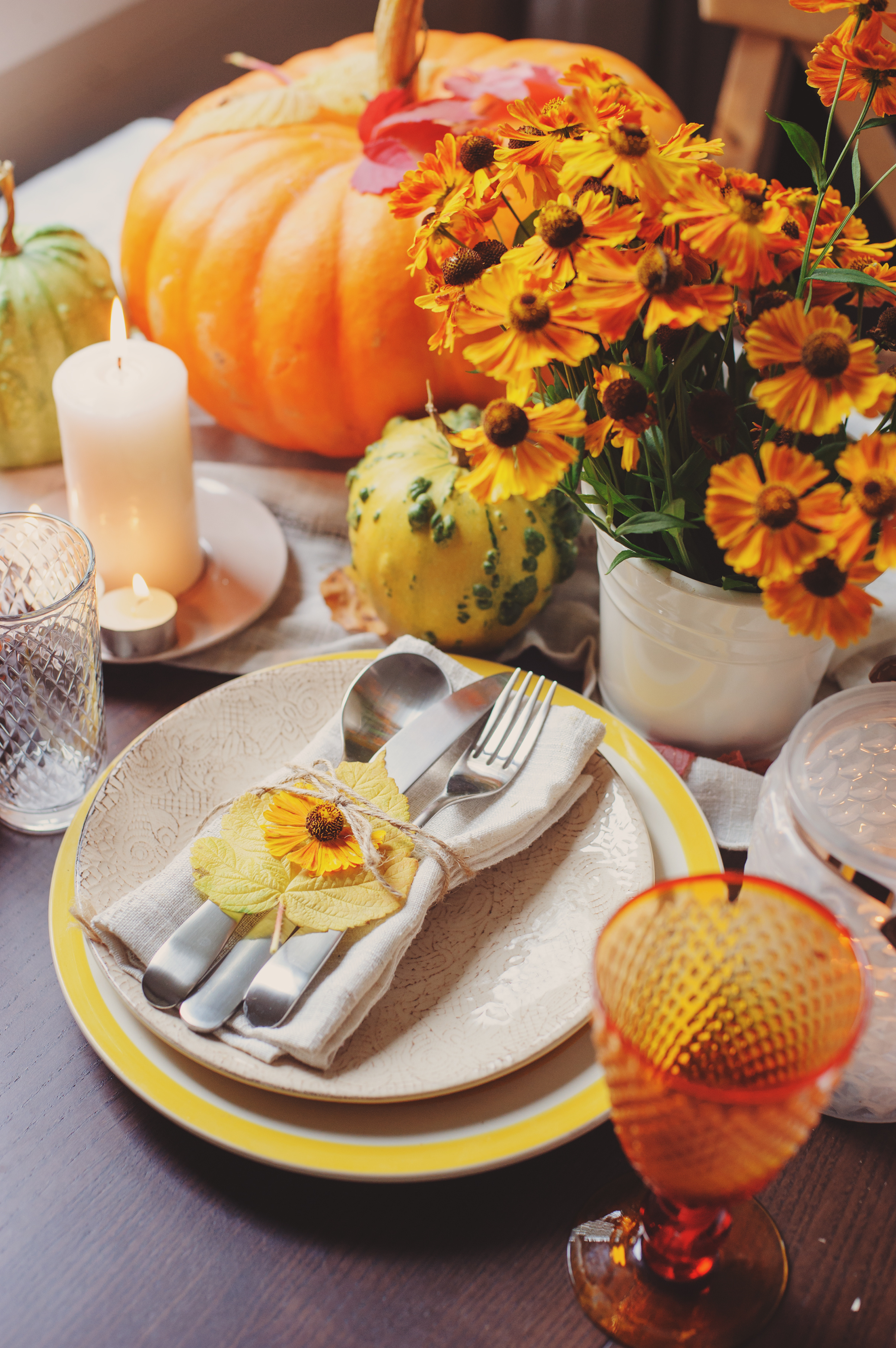 autumn traditional seasonal table setting at home with pumpkins, candles and flowers. Family celebrating Thanksgiving day.